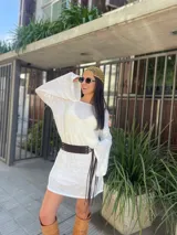 Vestido corto blanco traslúcido con mangas largas acampanadas, cinturón ancho marrón con flecos y sombrero de paja.