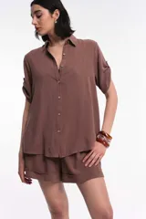 Conjunto de camisa y short color marrón, de tela rústica. La camisa es de corte recto, con cuello clásico, mangas cortas con presilla y cierre frontal con botones.