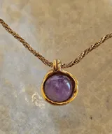 Collar con cadena de eslabones dorados y dije redondo con piedra amatista engarzada en metal dorado.