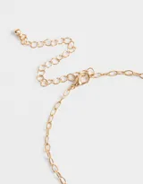 Collar corto con cadena dorada y dijes colgantes: espiral dorado, cristal blanco y trébol dorado.