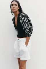 Top negro de escote pico con detalle de fornitura y mangas 3/4 abullonadas con estampado de flores bordadas.