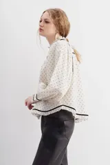 Camisa cruda de algodón con calce relajado y cuello redondo. Detalles de velvet negro y broderie en escote, puños y ruedo.