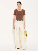 Pantalón de cuero ovino color crema, de silueta amplia y pata ancha. Tiene bolsillos con remaches en la parte delantera y cierre con botón jeanero y cremallera.
