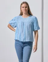 Blusa celeste de gasa marca Zac & Rachel, con cuello redondo, frunces en el frente, mangas 3/4 con puño, abertura central en la espalda y botón.