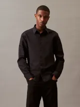 Camisa negra de lino y algodón, de corte clásico, con cuello en punta, cierre frontal con botones y mangas largas con puños abotonados.