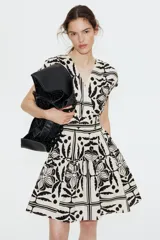 Vestido corto sin mangas de algodón color crudo con estampado de flores, hojas y lunares en negro. Tiene escote cruzado en V, cintura elastizada y falda con vuelo.