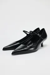 Zapato de cuero negro con tacón kitten, tira delantera con hebilla ajustable y punta fina.