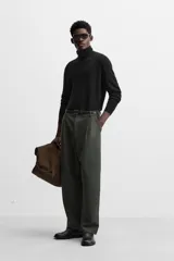 Pantalón relaxed fit color verde oscuro, con pliegues en la parte delantera, bolsillos laterales y traseros de ojal. Cierre frontal con cremallera y botón.