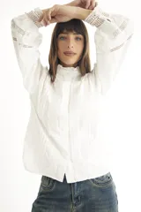 Camisa blanca de estilo romántico con cuello alto, mangas largas abullonadas y detalles de broderie.