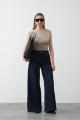 Top sin mangas color beige, confeccionado en tejido acanalado. Presenta hombreras definidas y un recorte fruncido bajo el busto que ajusta la silueta.