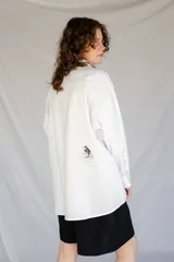Camisa blanca de algodón con cuello con lengüeta y botón labrado, manga larga con puños y botones, corte oversize y estampado de aves en el delantero.