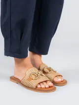 Sandalias bajas color beige con diseño tejido y detalle de hebilla dorada.