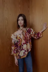 Blusa estampada con flores en tonos rosa, naranja y marrón, con mangas 3/4 con volados y lazo en el cuello.