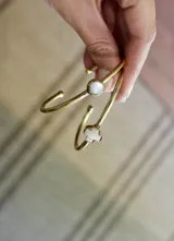 Pulsera rígida dorada con una piedra redonda de nácar en el centro.