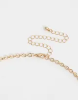 Collar corto dorado con cadena de eslabones gruesos y dijes colgantes: cristal facetado azul, dije dorado con forma de abanico, dije ovalado blanco con corazón dorado y strass, perla rosa y perla blanca.