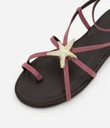 Sandalia plana color rosa con tiras finas, puntera redonda y adorno de estrella de mar dorada.