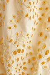 Vestido color crema a la rodilla, de tejido liviano de algodón con cuello redondo, botones ocultos adelante y cinturón fino extraíble. Mangas al codo abullonadas en broderie con puños elásticos.