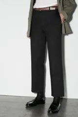 Pantalón de vestir color beige, de tiro alto y corte recto. Incluye cinturón marrón con hebilla metálica. Presenta bolsillos laterales y falsos bolsillos traseros de doble vivo. Cierre frontal con cremallera, botón interior y gancho oculto.