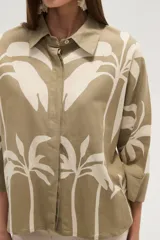 Camisa blanca con estampado de palmeras en color azul marino, de corte holgado, con cuello camisero, cierre frontal con botones y mangas 3/4 con puños anchos.