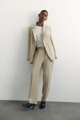 Blazer color beige de corte holgado con solapas de muesca, hombreras, abertura y botón en los puños, bolsillos delanteros ribeteados y bolsillo superior ribeteado. Forrado.