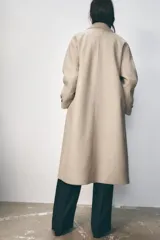 Abrigo largo color beige de cuello solapa y manga larga con trabilla y botón. Tiene bolsillos de vivo en el delantero y cierre frontal cruzado con botones.