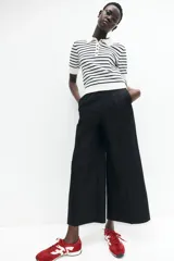 Pantalón palazzo negro de tiro alto con elástico oculto en la cintura, cierre lateral oculto y pinzas que realzan la figura. Modelo de corte holgado con bolsillos al bies, bolsillos decorativos atrás y piernas tres cuartos con raya adelante y atrás.