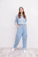 Camisa de denim azul con cuello clásico, cierre frontal con botones blancos, mangas largas con puños abotonados y dos bolsillos cargo con solapa en el pecho.