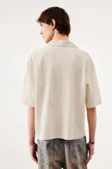 Camisa de manga corta color crema en tejido sirsaca de algodón. Modelo boxy con cuello abierto, tapeta lisa, bolsillo superior y bajo recto. Corte holgado.