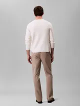 Pantalón chino de corte slim color beige, confeccionado en algodón y elastano. Presenta cierre con cremallera y botón, diseño clásico de cuatro bolsillos y logo de Calvin Klein bordado en la parte posterior.