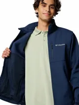Chaqueta softshell Columbia para hombre, color azul marino, con cierre frontal, cuello alto y múltiples bolsillos con cremallera. Presenta puños y dobladillo ajustables.