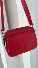 Bandolera negra de cuero sintético con doble bolsillo principal, un bolsillo frontal y trasero. Incluye correa ajustable.