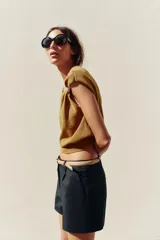 Top dorado de tejido de punto con cuello barco, sin mangas y detalle de fornitura metálica en el hombro.