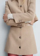 Chaqueta corta color beige de tweed con cuello camisero y cierre frontal con botones metálicos.