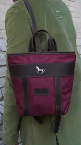Mochila pequeña color borgoña con detalles en cuero marrón, asa de mano y correas ajustables.