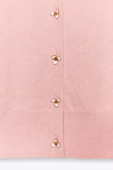 Chaqueta rosa de punto con cuello redondo y manga larga. Tiene hilo metalizado y cierre frontal con botones en relieve con forma de flor.