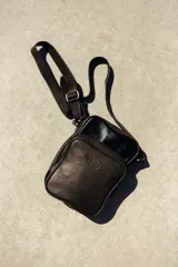Bandolera negra de cuero con correa ajustable, cierre superior y bolsillo externo con cierre. Incluye bolsillo interno y logo de la marca grabado en el frente.