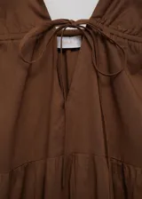 Vestido largo color marrón, con escote de pico y tirantes finos. Presenta un corte evasé y detalles fruncidos. El escote tiene un cierre de lazo.