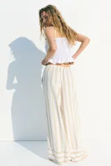 Pantalón de lino color crudo con rayas verticales color beige. Corte holgado, cintura elástica con cordón ajustable y piernas anchas extralargas.