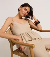 Blusa sin mangas color beige, con escote en V, breteles finos ajustables y peplum con volados en el bajo. Presenta lastex fruncido en la espalda.