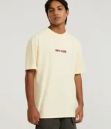 Remera de algodón color amarillo pálido, corte relajado y cuello redondo, con un pequeño estampado en el pecho con el texto "Heat Club" en tipografía estilizada color bordó.