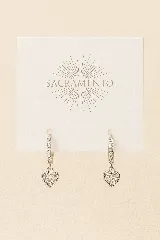 Par de caravanas plateadas con aros pequeños con incrustaciones de strass y dije colgante en forma de corazón con strass.