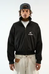 Chaqueta deportiva negra con cierre frontal, cuello alto y puños y cintura de elástico negro. Presenta franjas blancas en los hombros y el logo de Scuffers bordado en blanco en el pecho.