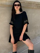 Remera negra de corte holgado con mangas cortas con volados y detalle de apliques de piedras en los volados.