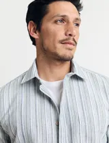 Camisa de manga corta a rayas verticales en tonos celeste, verde y blanco, con cuello clásico y bolsillo en el pecho. Cierre frontal con botones. Corte recto.