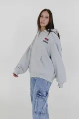 Canguro gris con capucha y bolsillo delantero tipo canguro. Estampado en el pecho con el logo de la marca Pulau en negro y rojo.