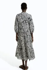 Vestido midi con estampado de hojas en blanco y negro, cuello mao, escote en V con botones, mangas globo tres cuartos con puños finos y falda acampanada con fruncido escalonado.