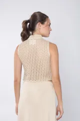 Top tejido color beige con espalda calada y cuello mao. Presenta cierre frontal con cordones y detalle de broches decorativos en el cuello.