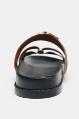 Sandalia plana de serraje color marrón, con dos tiras cruzadas en la parte delantera y una tira ancha con hebilla metálica ajustable.