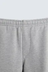 Pantalón jogger gris de corte recto, confeccionado en tejido de algodón compacto con interior en rizo. Tiene cintura elástica ajustable con cordón interior, bolsillos frontales y bolsillo de doble vivo en la espalda.