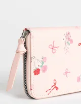 Billetera de cuerina color crema con estampado de flores y moños. Tiene formato rectangular, cierre circundante con tirador y múltiples compartimentos internos.